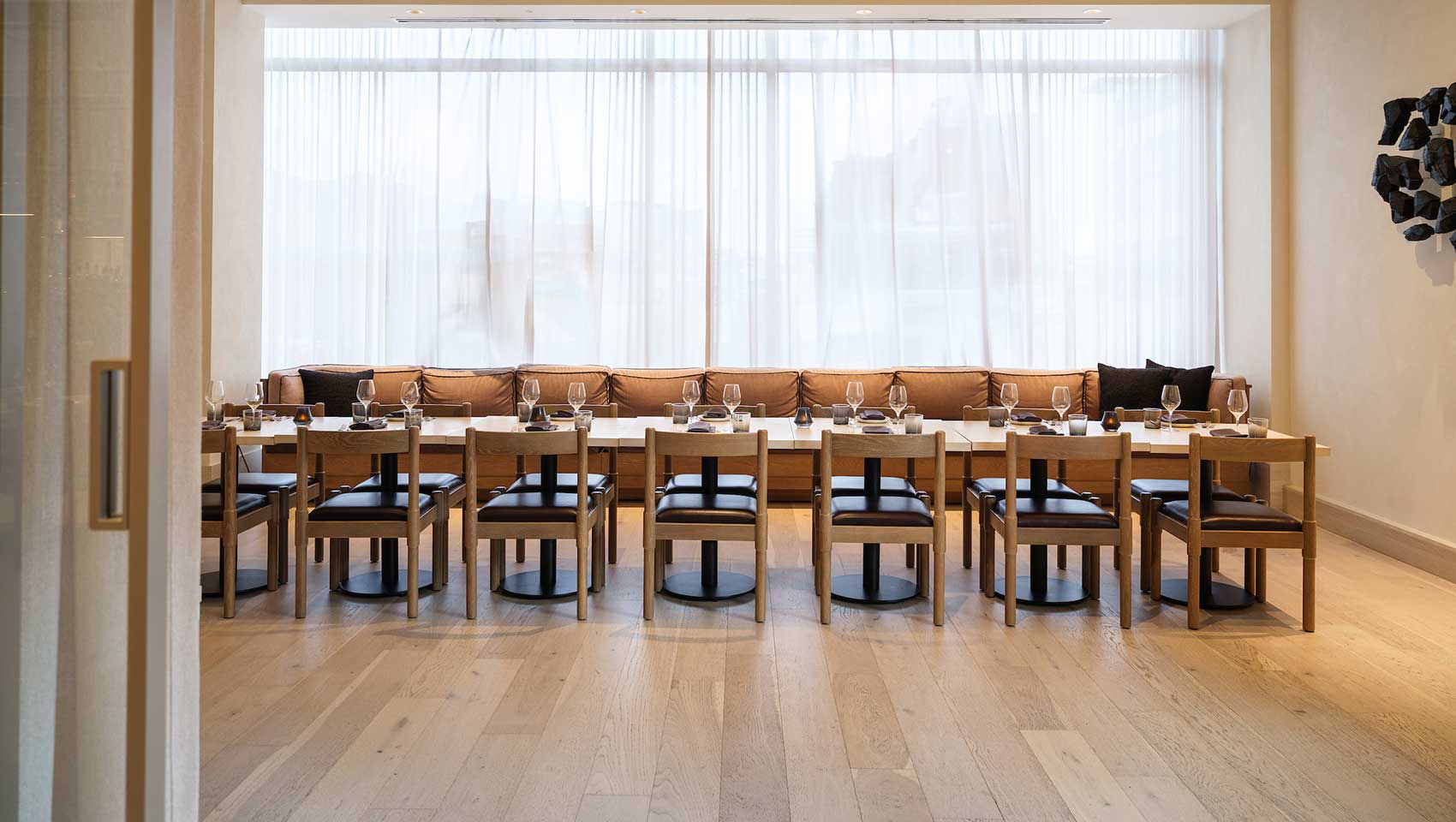 Private dining room with glass door closure, wall of windows and long table with chairs on either side