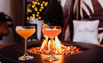 2 cocktails on a fire pit with twinkle lights blurred in the background